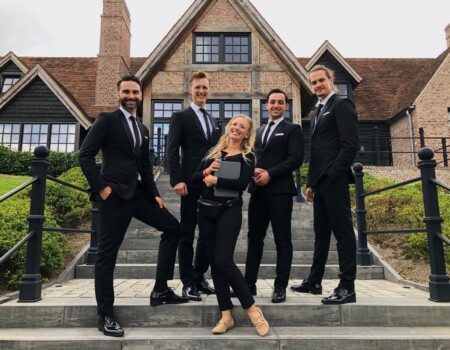 Groepsfoto van The Dutch Tenors in smoking op de trap, met manager Roos in het midden